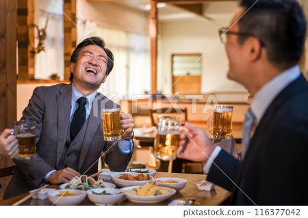 A middle-aged businessman laughing out loud at a year-end party, New Year's party, drinking party, or banquet at an izakaya 116377042