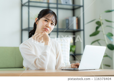 使用一台電腦在客廳裡的年輕女子 116378404