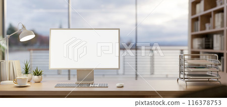A computer with a white-screen mockup on a wooden table in a modern office with an ocean view. 116378753