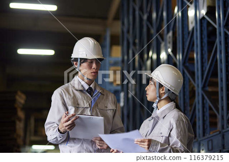 Men and women in work clothes having a meeting at a factory 116379215