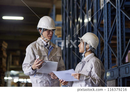 Men and women in work clothes having a meeting at a factory 116379216