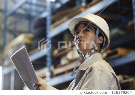 A female engineer in a helmet inspects the shelves in the warehouse. A female engineer in a helmet inspects the shelves in the warehouse. 116379264