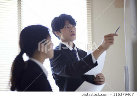 一名男性和一名女性辦公室職員在會議室一邊展示文件一邊進行解說。 一名男性和一名女性辦公室職員在會議室一邊展示文件一邊進行解說。 116379407