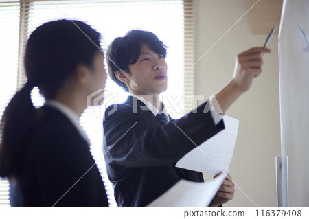 一名男職員和他的女同事一邊指著白板一邊解釋著什麼。 一名男職員和他的女同事一邊指著白板一邊解釋著什麼。 116379408