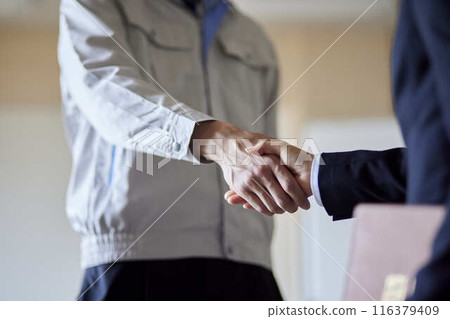一名身穿工作服的男子和身穿西裝的女子握手。 一名身穿工作服的男子和身穿西裝的女子握手。 116379409
