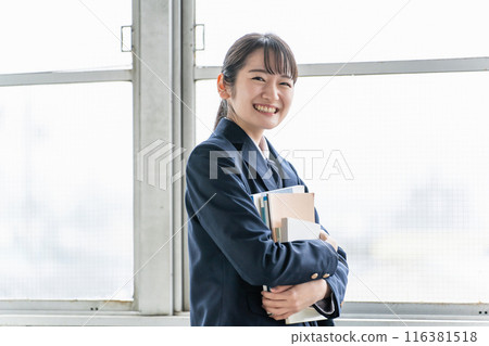 一個穿著制服的女學生在教室裡拿著教科書 116381518