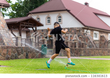 Young white boy running under the water from the sprinkler 116381613