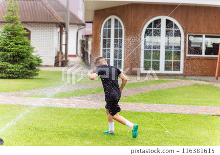 Young white boy running under the water from the sprinkler 116381615