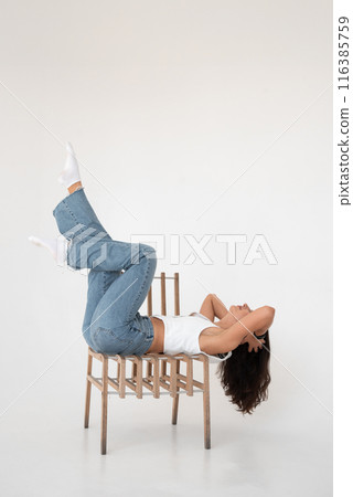 Happy beautiful girl posing with a chair in a new hot look. Wearing blue jeans and white waistcoat 116385759