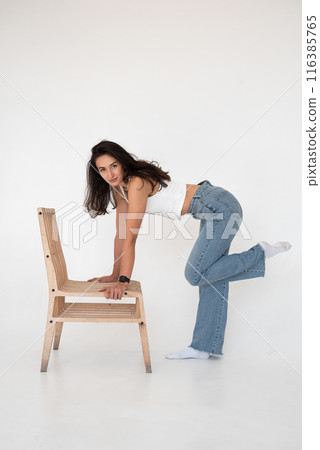 Happy beautiful girl posing with a chair in a new hot look. Wearing blue jeans and white waistcoat 116385765