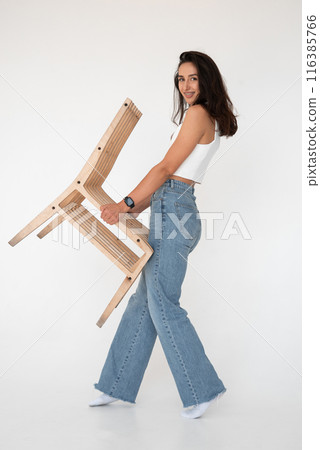 Happy beautiful girl posing with a chair in a new hot look. Wearing blue jeans and white waistcoat 116385766