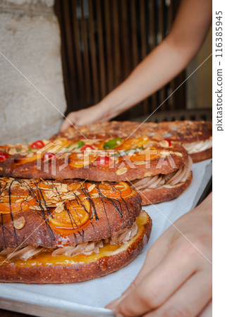 Close-up of a woman holding a tray with traditional cokes fresh from the oven. Vertical Close-up of a woman holding a tray with traditional cokes fresh from the oven. Vertical 116385945