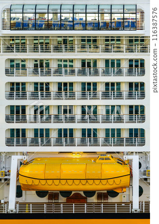 Side view of yellow lifeboat and balconies on a large high cruise ship, ship safety equipment Side view of yellow lifeboat and balconies on a large high cruise ship, ship safety equipment 116387576