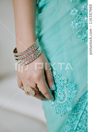 Female hand with diamond rings and bracelet leaning turquoise patterned dress 116387668