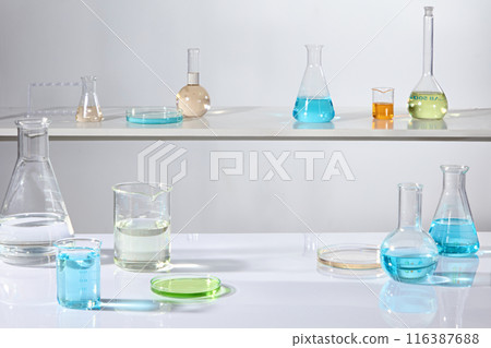 Several types of laboratory equipments placed on laboratory shelf against white background, containing colorful liquid. Front angle view photo with blank space in the center for product showing 116387688