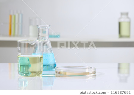 Close up shot at the white table top containing some lab glassware consist of an erlenmeyer of blue liquid, a beaker and a petri dish. Lab concept photo for product advertising, copy space 116387691