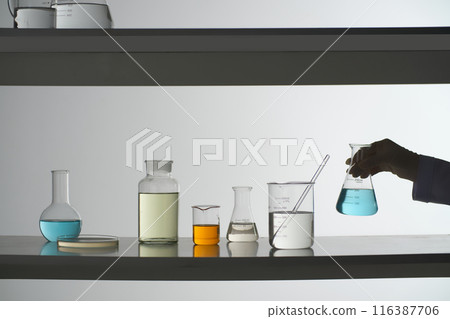 Creative template photo to design advertising pic. The scientist prepare to put the erlenmeyer of blue fluid on the second tier of the lab shelf, next to other glassware Creative template photo to design advertising pic. The scientist prepare to put the erlenmeyer of blue fluid on the second tier of the lab shelf, next to other glassware 116387706