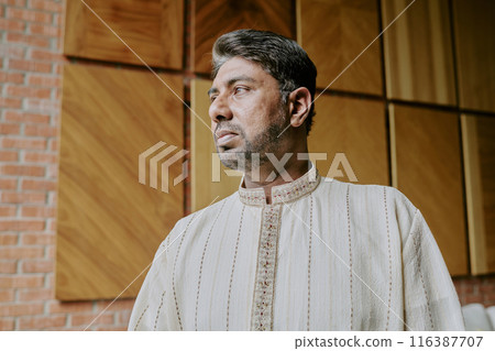Low angle shot of adult Indian man dressed in creamy flax shirt standing still and looking away 116387707