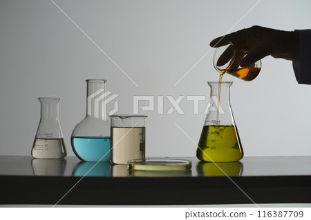 The advertising photo from front view, orange liquid in the beaker poured into an erlenmeyer flask, which placed on the table beside other lab glassware. Copy space for adding text 116387709