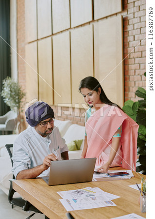 Highly skilled indian teamlead gesticulating wildly while demonstrating presentation to his young female colleague 116387769