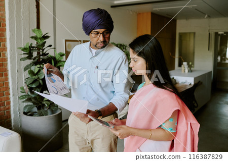 Teamlead showing last analytical results presented on papers while his young female employee listening to instruction and explanation carefully and taking notes using tablet Teamlead showing last analytical results presented on papers while his young female employee listening to instruction and explanation carefully and taking notes using tablet 116387829