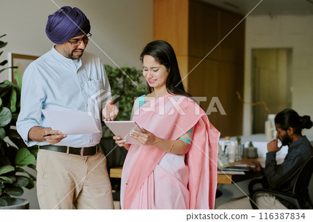 Indian colleagues comparing last financial report with launched presentation in tablet, other making presentation while sitting at table in blurred background 116387834