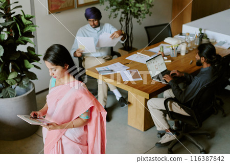 High angle shot of small group of IT specialist working with diagrams and database using different digital devices and sources of information 116387842