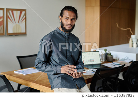 High skilled Indian worker sitting for photo while he holding white tablet in cozy office 116387922