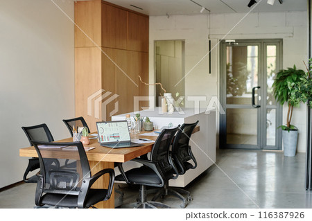 Spacious and light office equipped with wooden table and black chairs, digital devices brochures and decor items on table Spacious and light office equipped with wooden table and black chairs, digital devices brochures and decor items on table 116387926