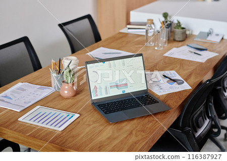 High angle shot of workplace equipped with digital devices and brochures with analytical diagrams and decor items High angle shot of workplace equipped with digital devices and brochures with analytical diagrams and decor items 116387927