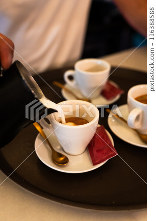 Waiter pouring milk into the coffee cup before serving it to the table. Vertical 116388588