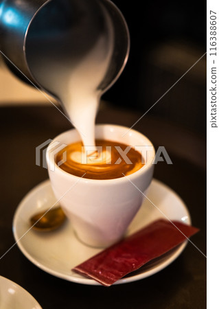 Milk pitcher pouring cream into a coffee cup. Vertical 116388607