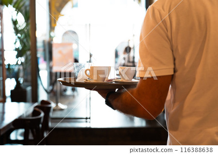 Waiter carrying coffees to a table with tray in one hand Waiter carrying coffees to a table with tray in one hand 116388638