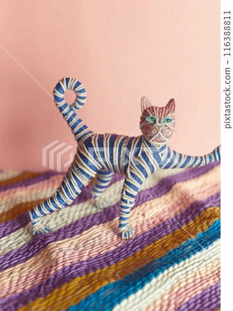 Blue and pink striped cat figurine standing on colorful textile Blue and pink striped cat figurine standing on colorful textile 116388811