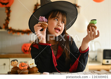 Cheerful little girl in witch costumes decorating Halloween cupcakes in the kitchen Cheerful little girl in witch costumes decorating Halloween cupcakes in the kitchen 116389401