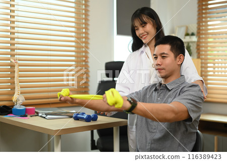 Male patient undergoing physical therapy with elastic bands at clinic. Rehabilitation concept. Male patient undergoing physical therapy with elastic bands at clinic. Rehabilitation concept. 116389423
