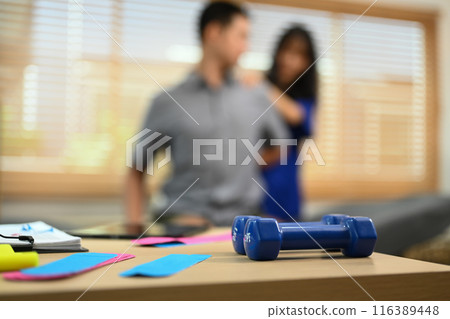 Kinesio tapes and dumbbells on table at physiotherapist office. Rehabilitation, treatment and healthcare concept Kinesio tapes and dumbbells on table at physiotherapist office. Rehabilitation, treatment and healthcare concept 116389448