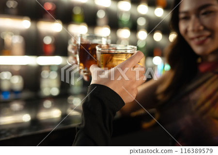 Close up shot of two friends toasting with drinks in the bar. Nightlife, celebrations and friendship concept 116389579