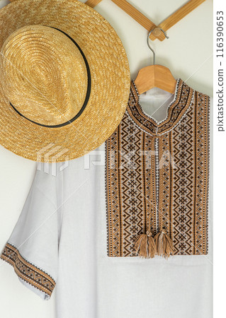 Ukrainian clothes embroidered shirt. Brown beige and white black threads background. Straw hat. Vyshyvanka symbol of Ukraine. Embroidery cross stitching. National Ukrainian stitch Traditional clothing Ukrainian clothes embroidered shirt. Brown beige and white black threads background. Straw hat. Vyshyvanka symbol of Ukraine. Embroidery cross stitching. National Ukrainian stitch Traditional clothing 116390653