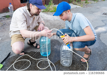 Dad and teenage son work together on the street near the garage. Outdoor activity. Family spend time. Helping and teach. Repairing a hose and pump for hand washing a car from a plastic bottle Dad and teenage son work together on the street near the garage. Outdoor activity. Family spend time. Helping and teach. Repairing a hose and pump for hand washing a car from a plastic bottle 116390666