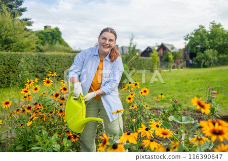 Happy woman taking care of flowers outdoors in garden, watering with can. Female preparing for preparing flowers for international women day. High quality photo Happy woman taking care of flowers outdoors in garden, watering with can. Female preparing for preparing flowers for international women day. High quality photo 116390847