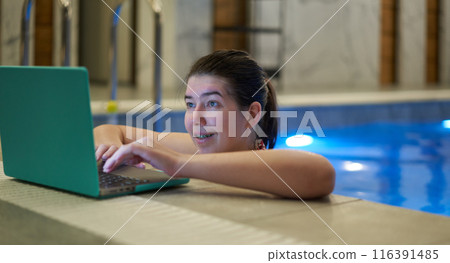 Woman Typing on Laptop with Smile in Swimming Pool 116391485