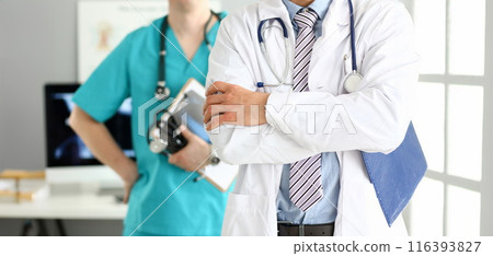 Male doctor with arms crossed on chest standing in line with colleagues in office 116393827