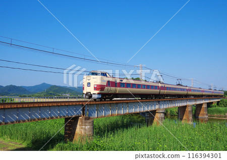 The last day of regular service, the JNR-colored 381 series Yakumo express train speeds across the Sanin Main Line railway bridge under a clear blue sky. 116394301