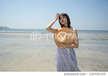 A woman standing on the beach with a straw hat (Yuigahama, Kanagawa Prefecture) 116395250