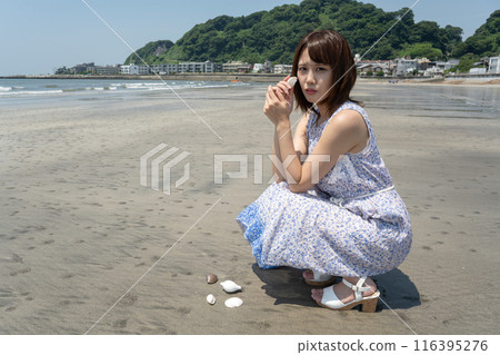 A woman squatting on the beach holding a seashell (Yuigahama, Kanagawa Prefecture) A woman squatting on the beach holding a seashell (Yuigahama, Kanagawa Prefecture) 116395276