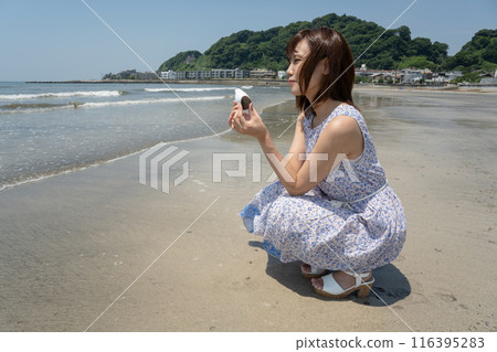 A woman squatting on the beach holding a seashell (Yuigahama, Kanagawa Prefecture) A woman squatting on the beach holding a seashell (Yuigahama, Kanagawa Prefecture) 116395283