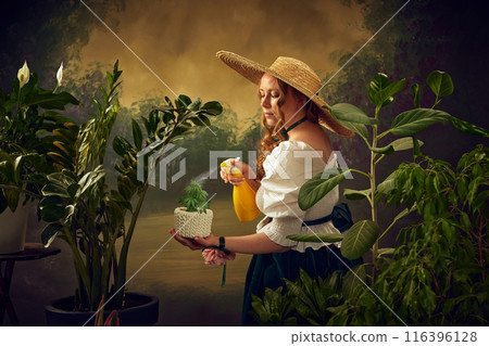 Gardening. Elegant woman in skirt, blouse and hat, sitting on chair in garden and spraying plants with water, against vintage background. Victorian summer vibe. Gardening. Elegant woman in skirt, blouse and hat, sitting on chair in garden and spraying plants with water, against vintage background. Victorian summer vibe. 116396128