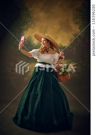 Elegant young woman in historical clothes, large straw hat taking selfie with mobile phone giant vintage background Elegant young woman in historical clothes, large straw hat taking selfie with mobile phone giant vintage background 116396280