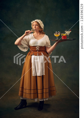Portrait of woman in historical attire, drinking cocktail and holding a tray with various alcoholic drinks, set against vintage green background 116396329